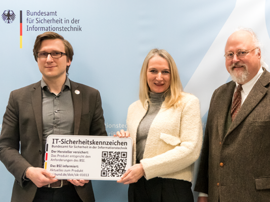 (v.l.n.r.): Joshu Wiebe übergibt das symbolische IT-Sicherheitskennzeichen an Maja von Bomhard und Sebastian von Bomhard.